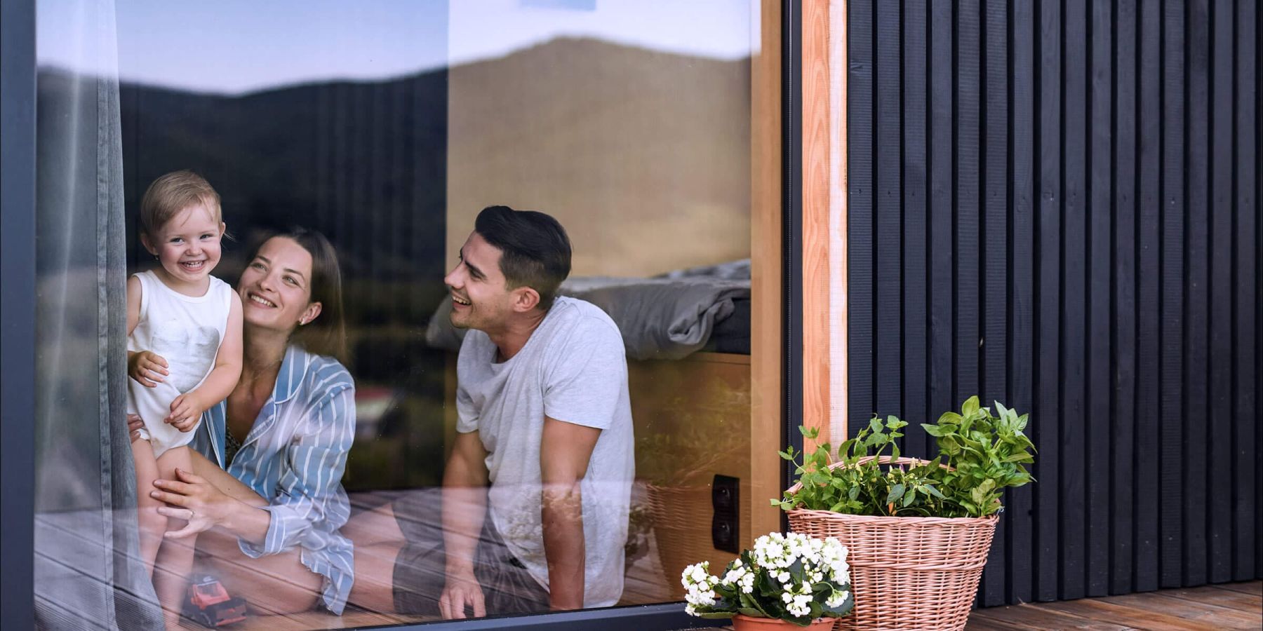 Junge, glückliche Familie mit Kleinkind schaut von der Verandatür Ihres eigenen Hauses in den Garten